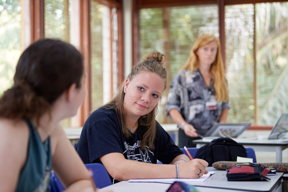 Image of a young woman at a desk, writing in a notebook.